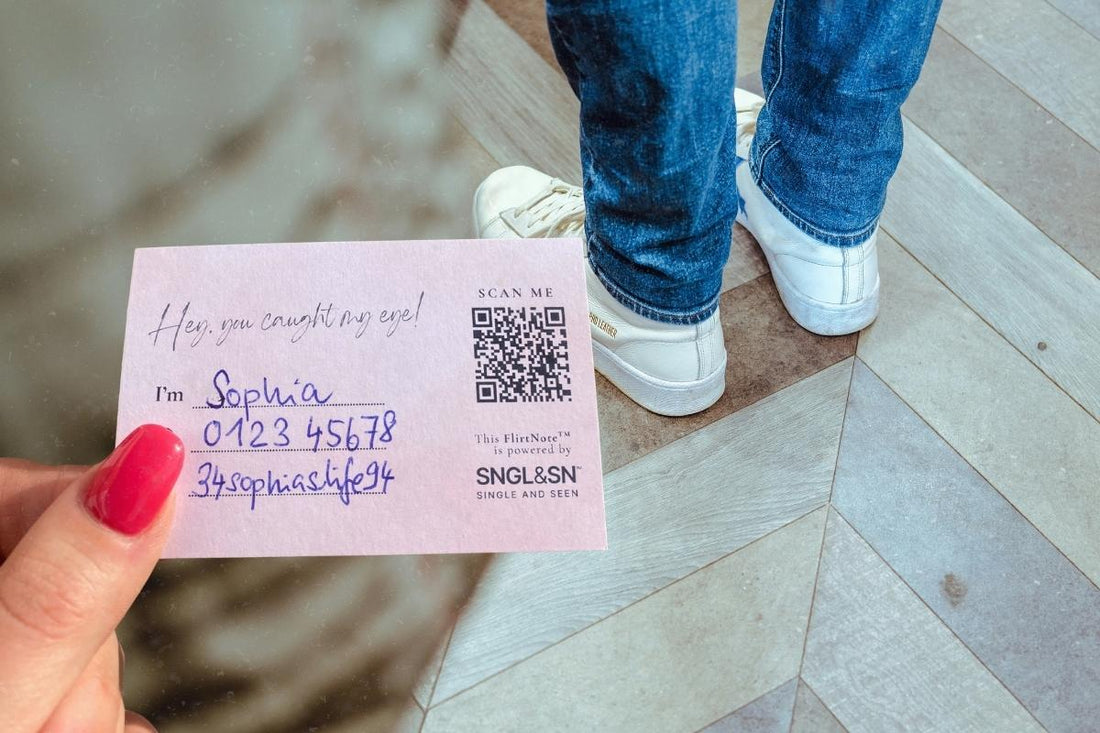 Woman holding a FlirtNote about to pass it to a man standing in line in front of her